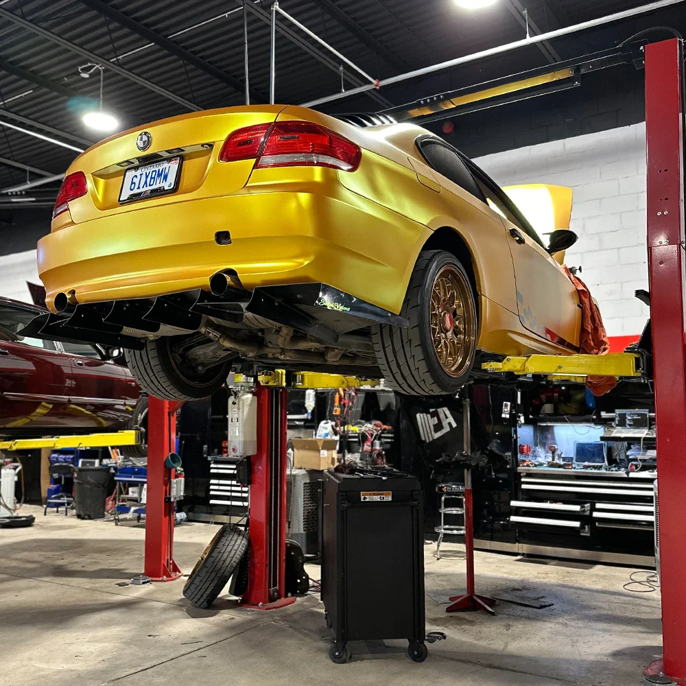 Yellow BMW M3 on hydraulic lift in auto repair shop.