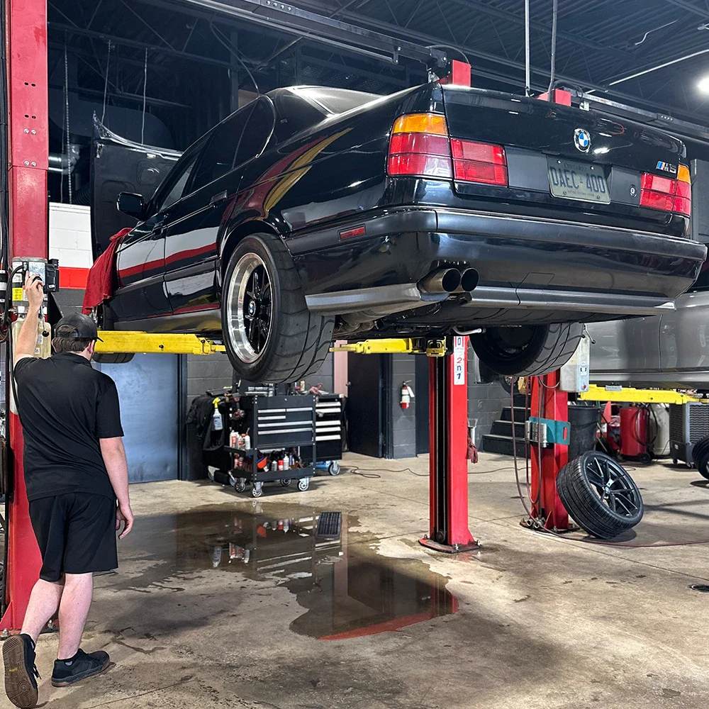 Black BMW car lifted in auto repair shop with mechanic nearby.