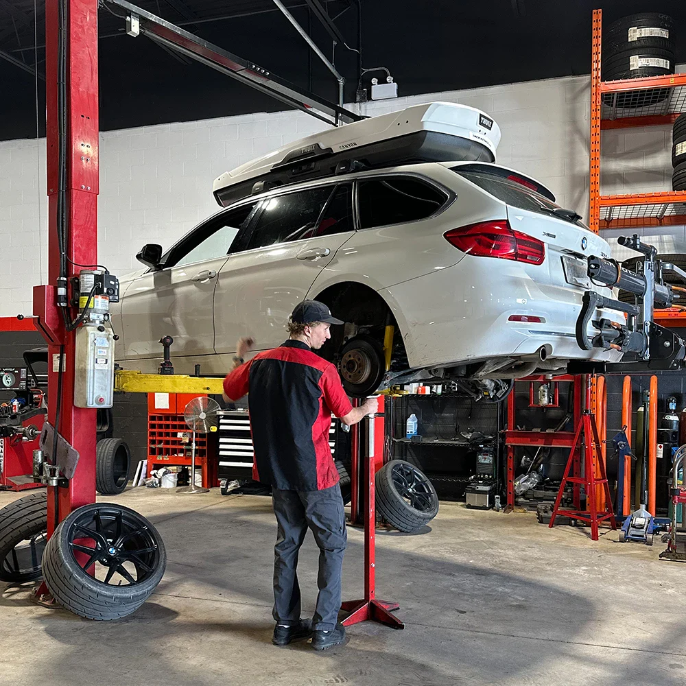 Mechanic working on a white SUV on hydraulic lift in auto repair shop.