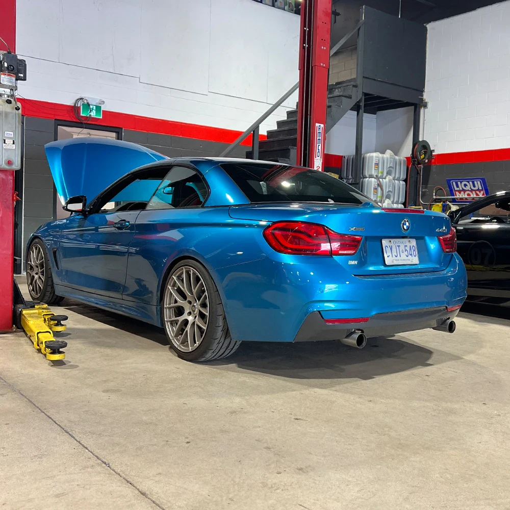 Blue BMW parked in workshop with open hood and custom wheels.