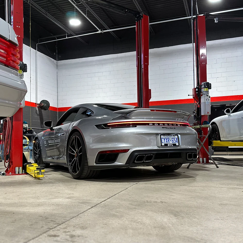 Silver Porsche 911 in automotive workshop with lift and tools.