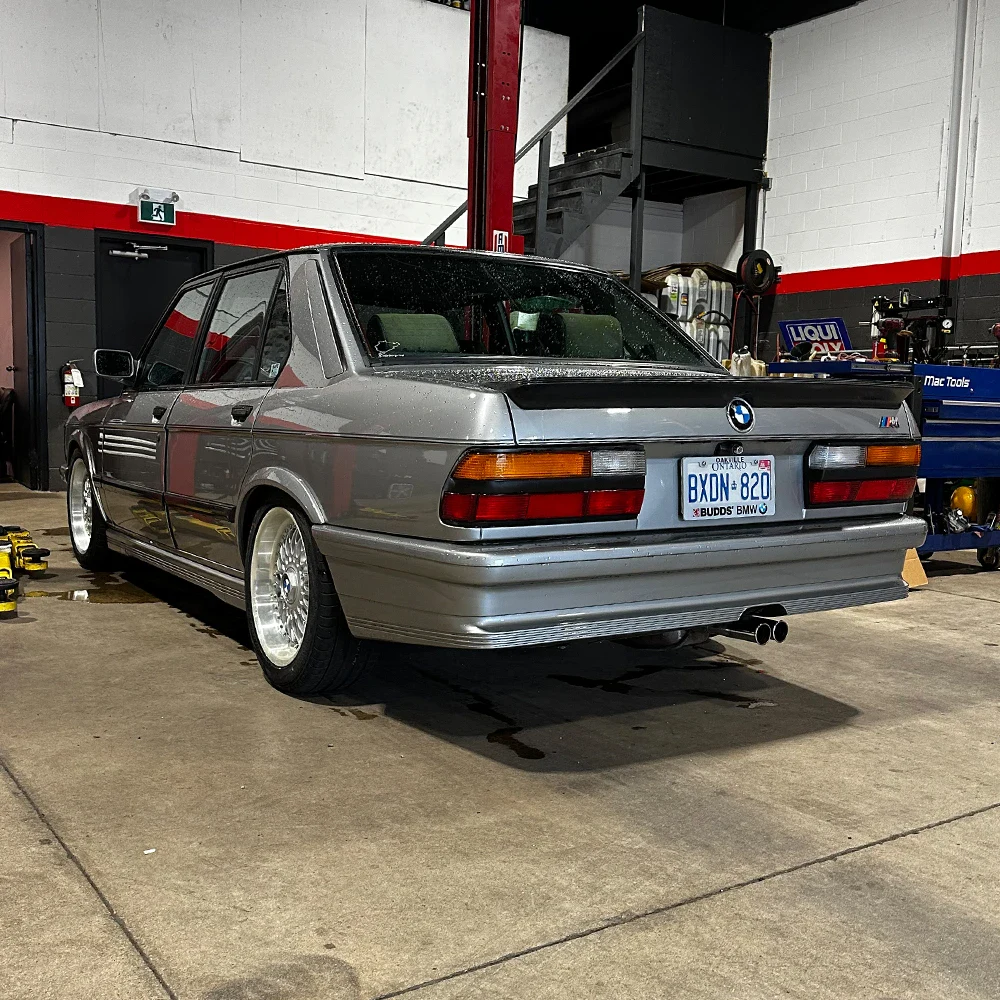 Classic BMW E30 in a garage with tools and equipment.