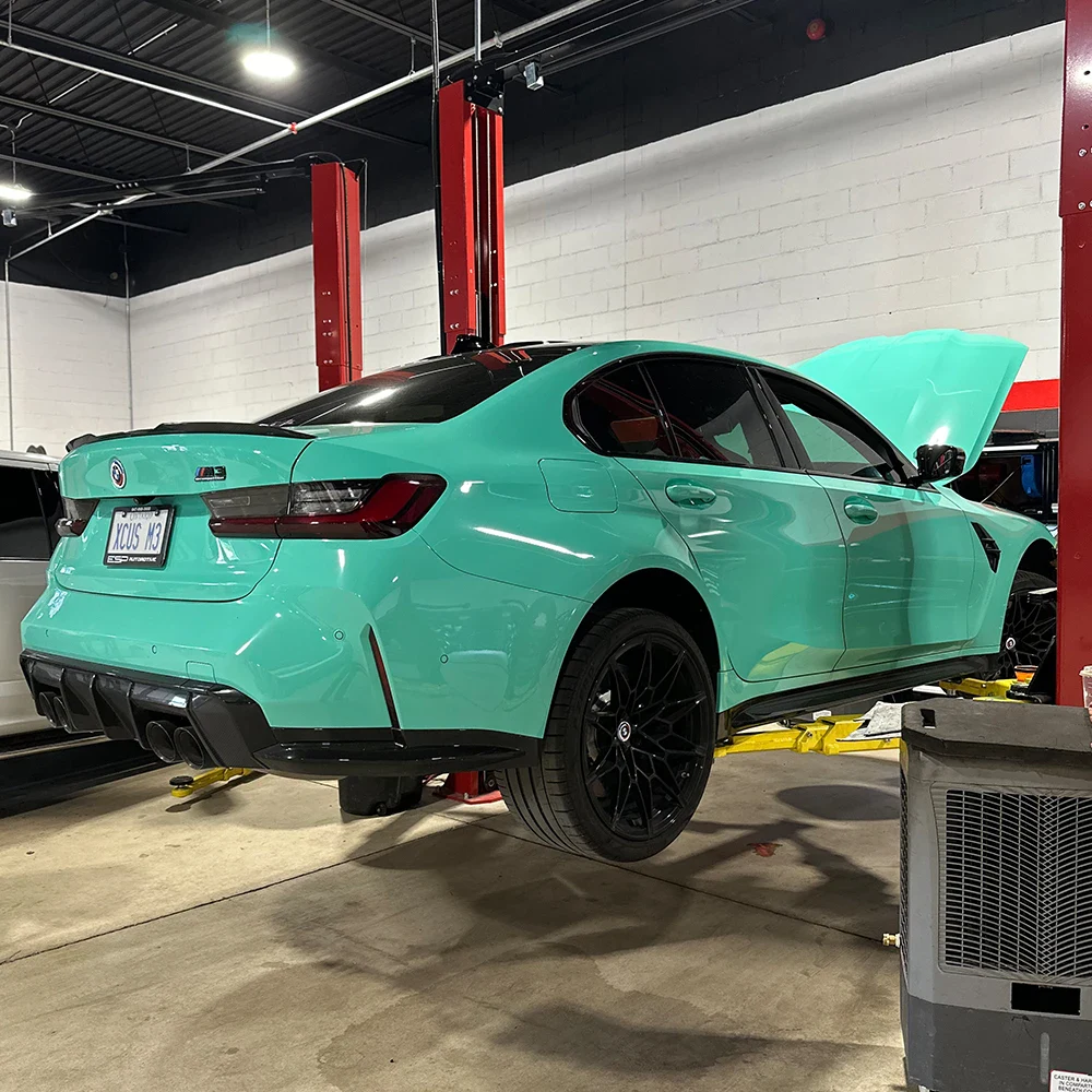Luxury green sedan with open hood in automotive workshop.