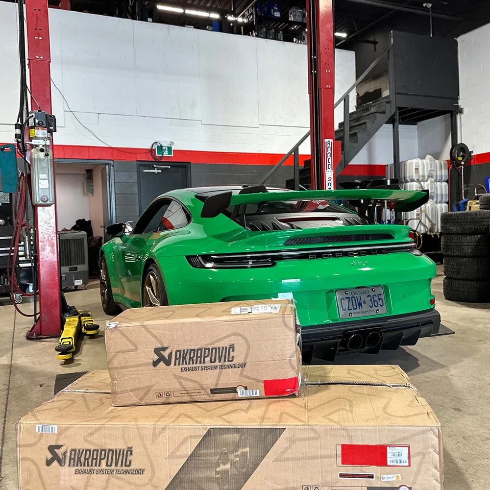 Green Porsche 911 sports car in automotive workshop with tools and tires.