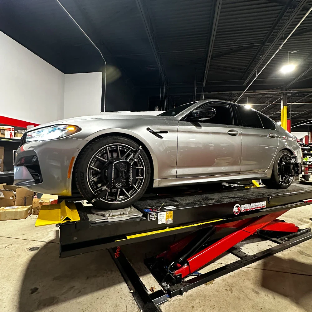 Silver luxury sedan on a hydraulic lift in an automotive workshop.