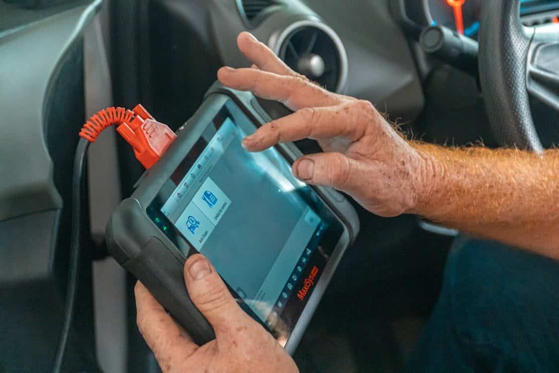Technician using diagnostic scanner in vehicle interior.