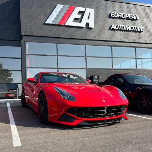 Red Ferrari sports car parked outside European Automotive dealership.