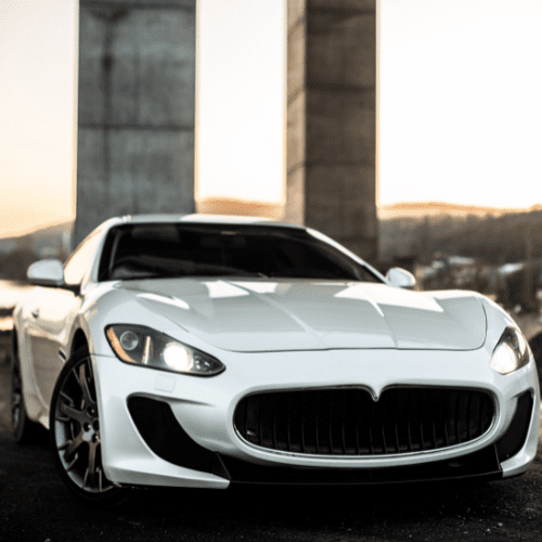 Luxury white sports car with sleek design parked under bridge at sunset.