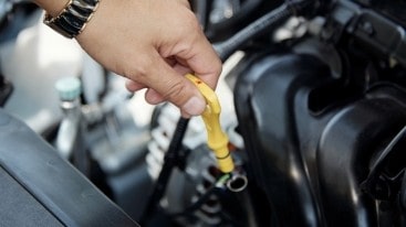 Technician inspecting engine oil level in vehicle at auto service center.