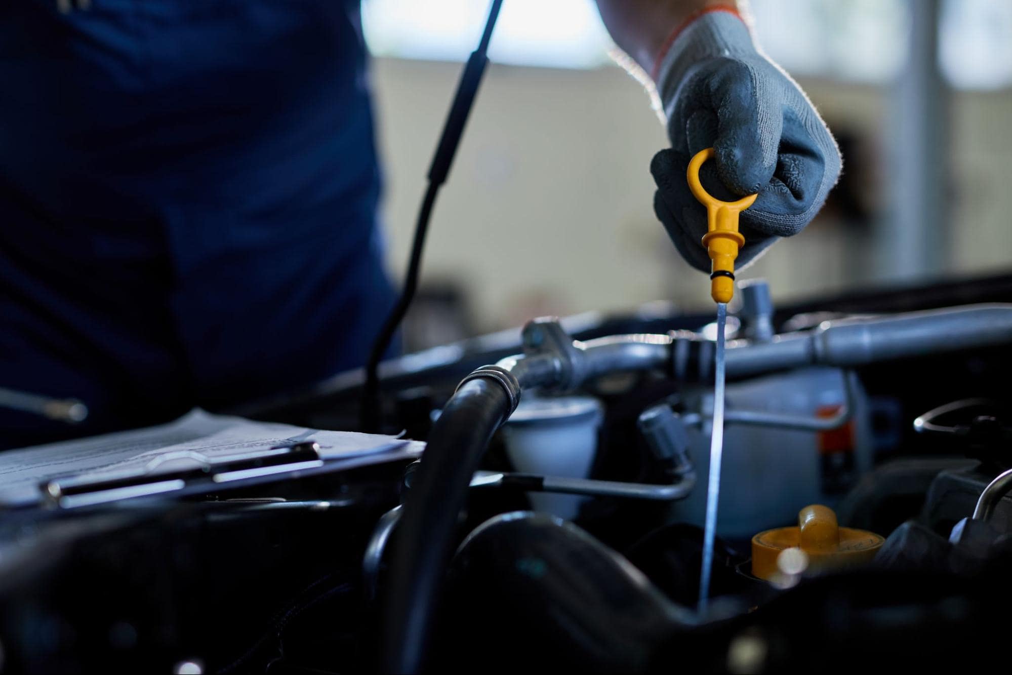 Technician checking engine oil level in a car engine with a dipstick.
