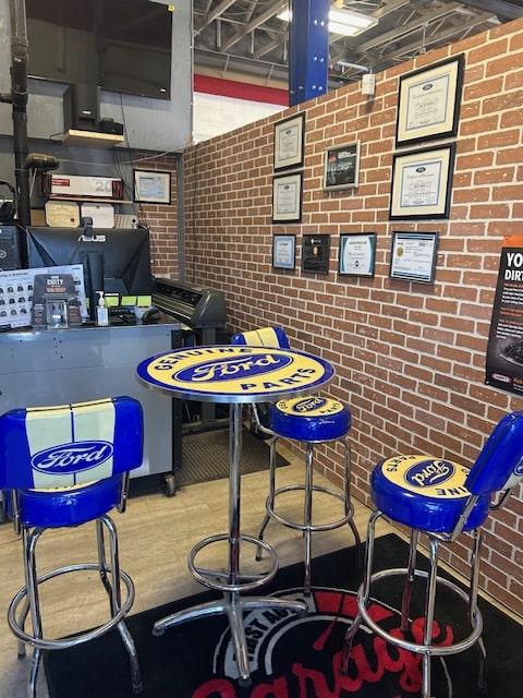 Ford-themed auto service lounge with branded chairs and certificates on brick wall.