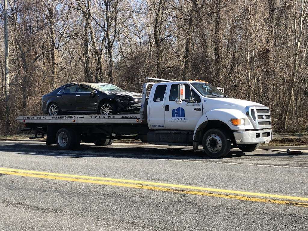 Tow truck transporting a damaged black car on a flatbed.