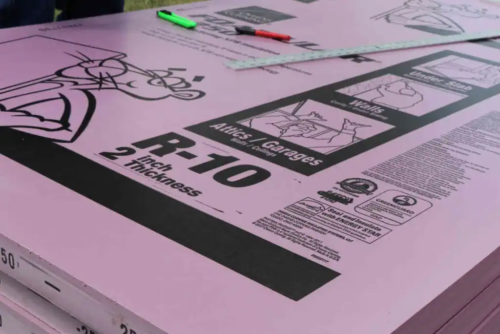 A close-up of pink foam board insulation sheets with installation instructions and tools on top.