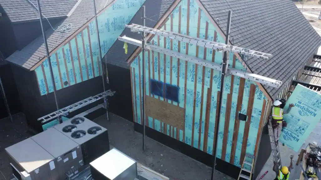 Construction workers installing insulation on a house exterior during building phase.