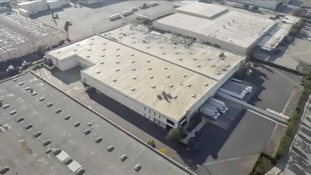 Aerial view of a commercial warehouse with ventilation units on the roof and surrounding parking area.