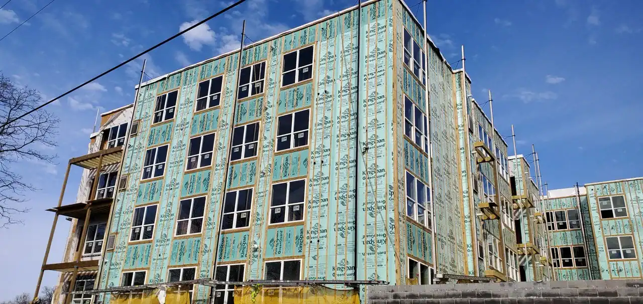 Under-construction multi-story building with insulation panels and scaffolding, blue sky background.