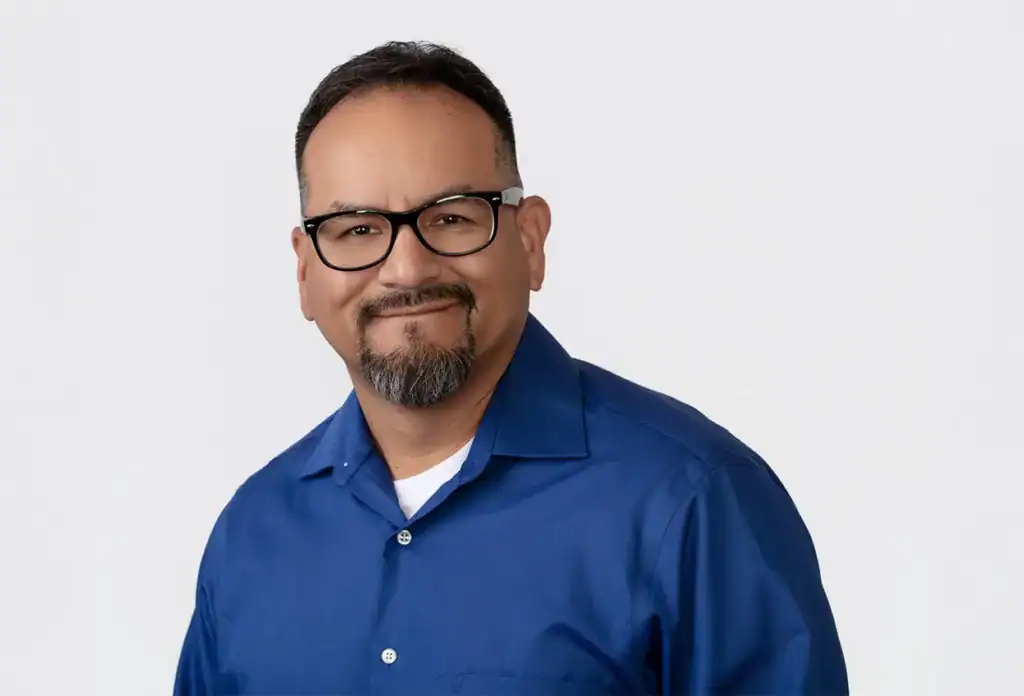 Smiling man in professional attire with glasses, looking confident and approachable.