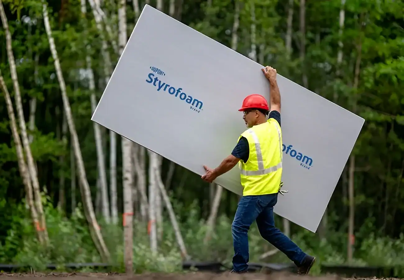 Worker installing Styrofoam insulation board outdoors.