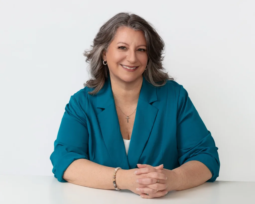 A woman smiling in a blue blazer, sitting at a white table, representing professional confidence and.