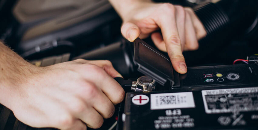 Person inspecting car battery under the hood during winter cold weather.