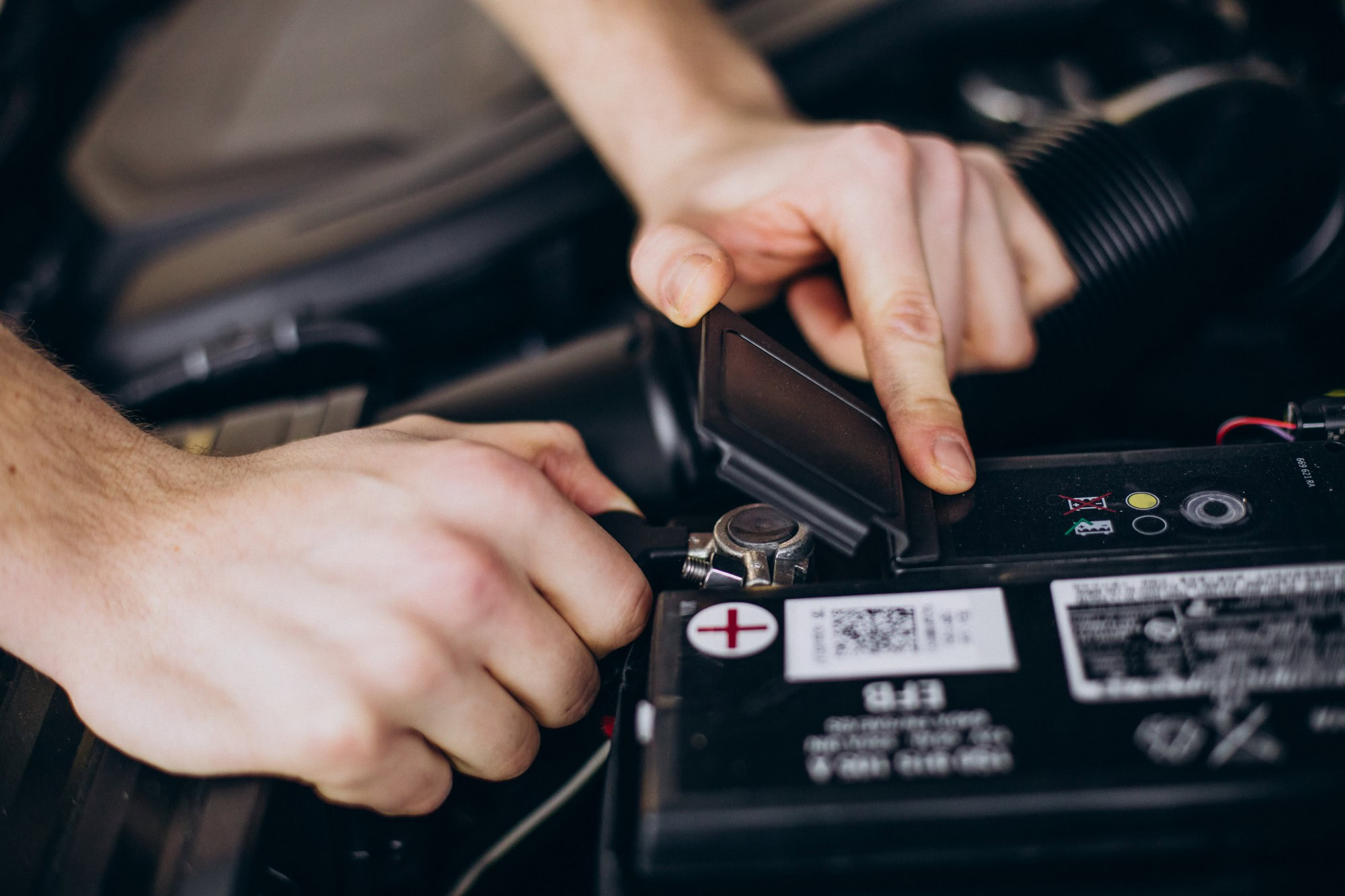 Person inspecting car battery under the hood during winter cold weather.