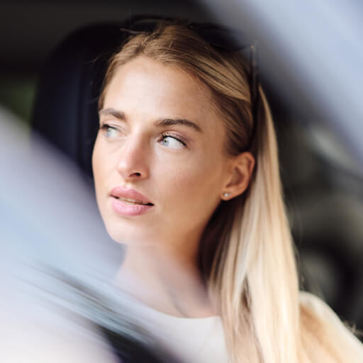 Young woman sitting in an electric vehicle, looking out thoughtfully.