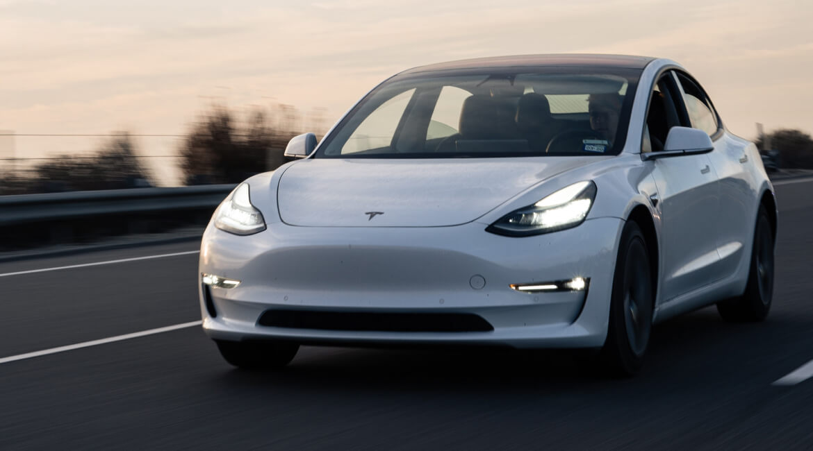 Tesla Model 3 electric vehicle driving on highway at sunset.