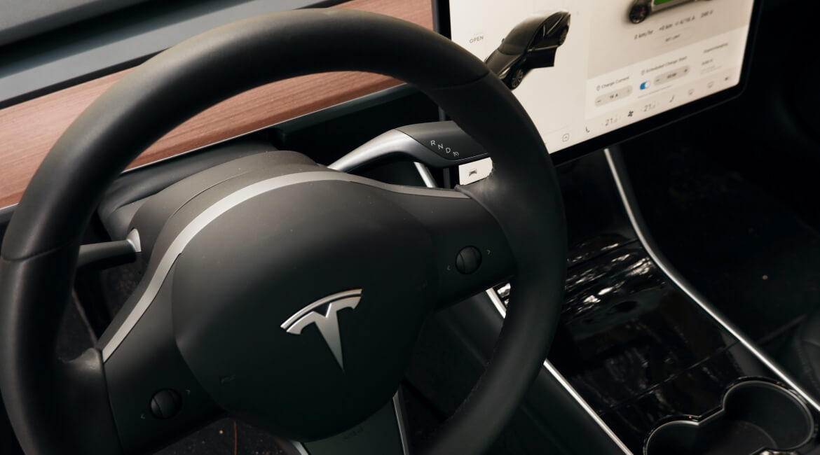 Tesla steering wheel and dashboard in electric vehicle interior.