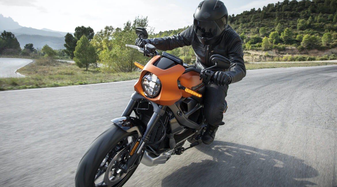 Motorcycle rider in black gear on an electric bike on a winding road.