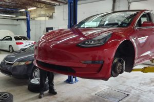 Red Tesla Model 3 on lift at Garage-EV in Dartmouth for maintenance.