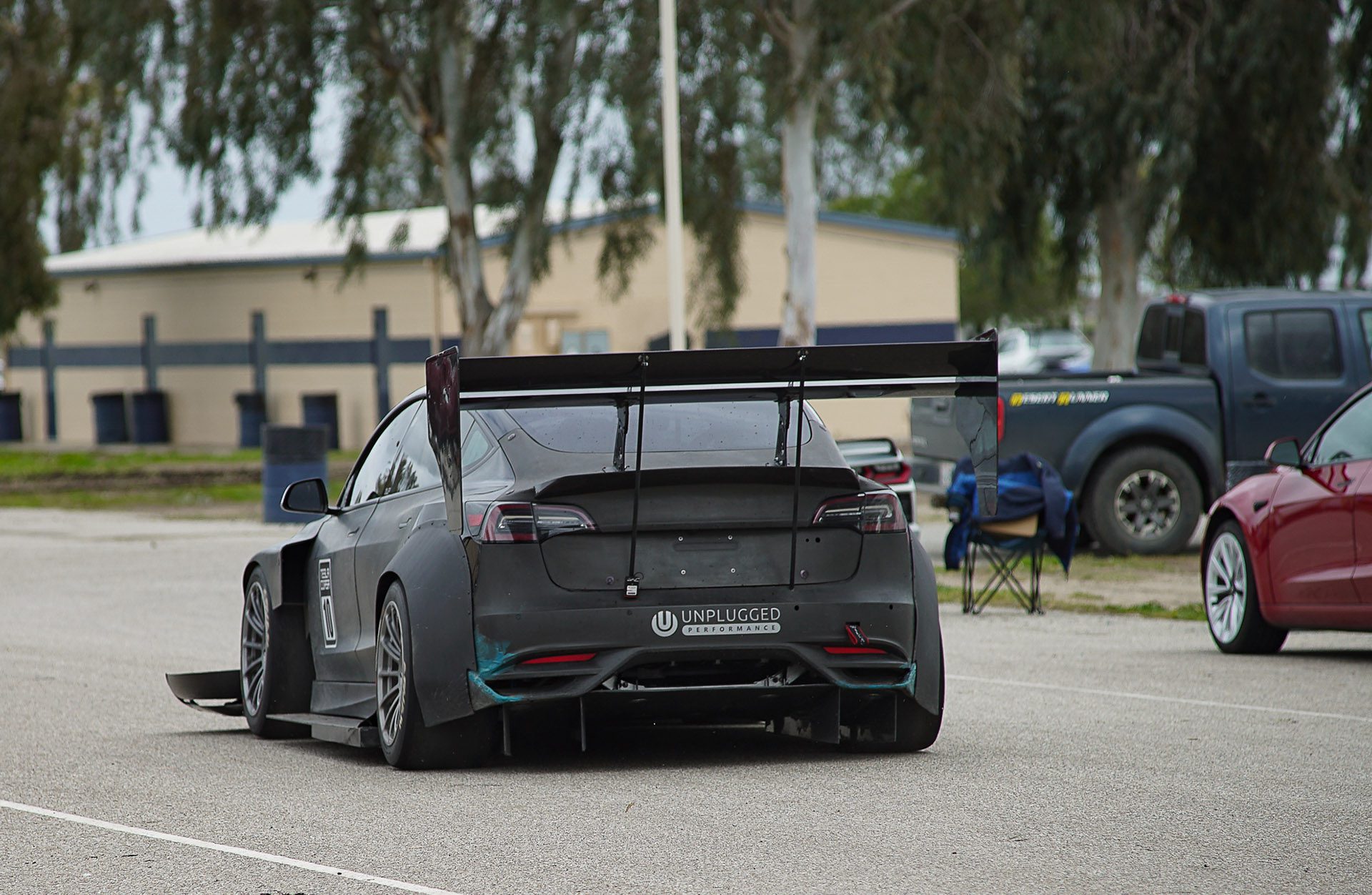 Modified electric car with aerodynamic rear wing in parking lot.