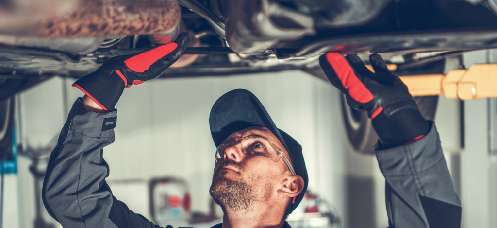 Automotive technician inspecting vehicle underside in garage.