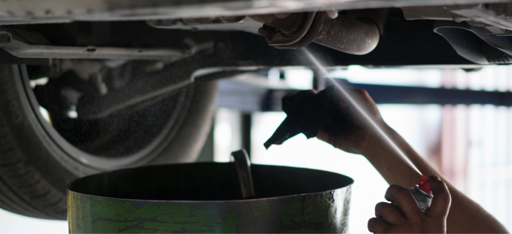 Technician applying undercoating to a vehicle's underside in a garage.