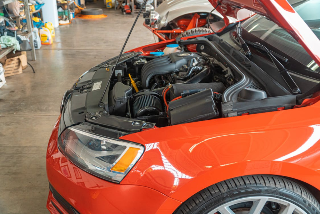 Red car with open hood showing engine at electric vehicle service center.