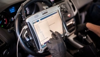 Technician performing vehicle diagnostics with a tablet inside a car.