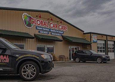 Exterior view of Global Car Care auto service center with parked cars, under cloudy sky.