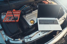 Automotive repair tools and laptop on car engine bay for diagnostics and maintenance.