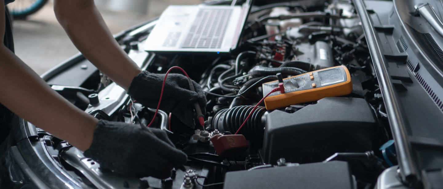 Engine diagnostics technician using multimeter on car engine.