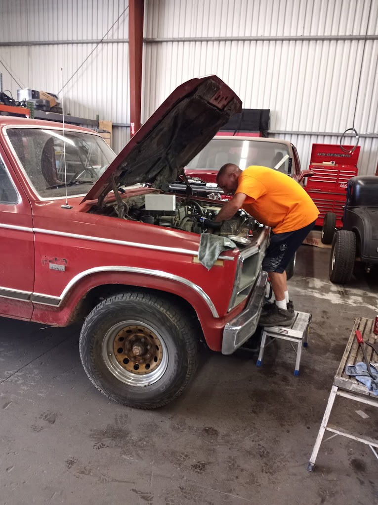 Vintage red hot rod with open hood, mechanic working on engine.