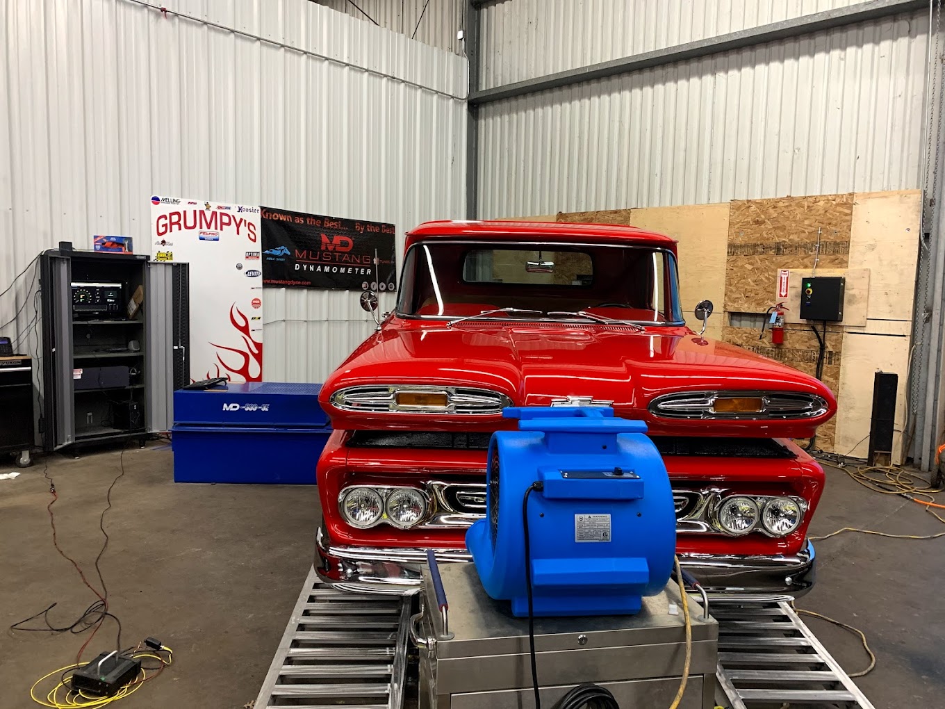 Vintage red hot rod in a workshop setting with engine testing equipment.