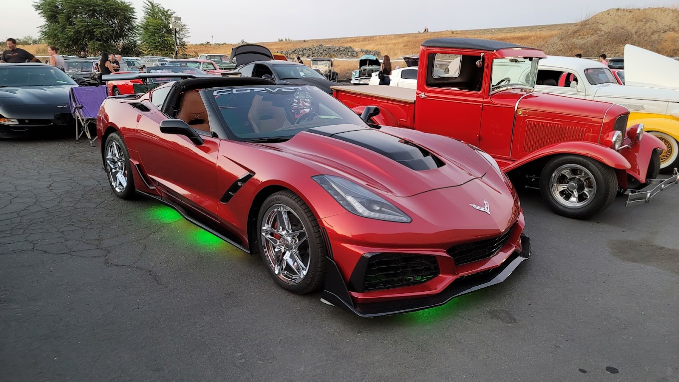 A sleek red Corvette Stingray with underglow lighting parked among classic cars at Grumpy's Hot Rod.