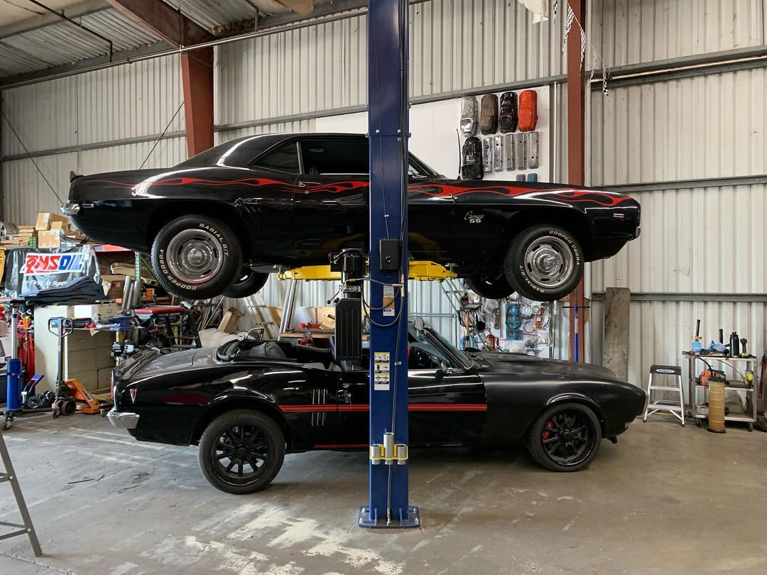 Classic black hot rod car lifted on a hydraulic lift in a garage.