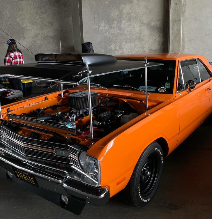 Classic orange muscle car with open hood at car show.