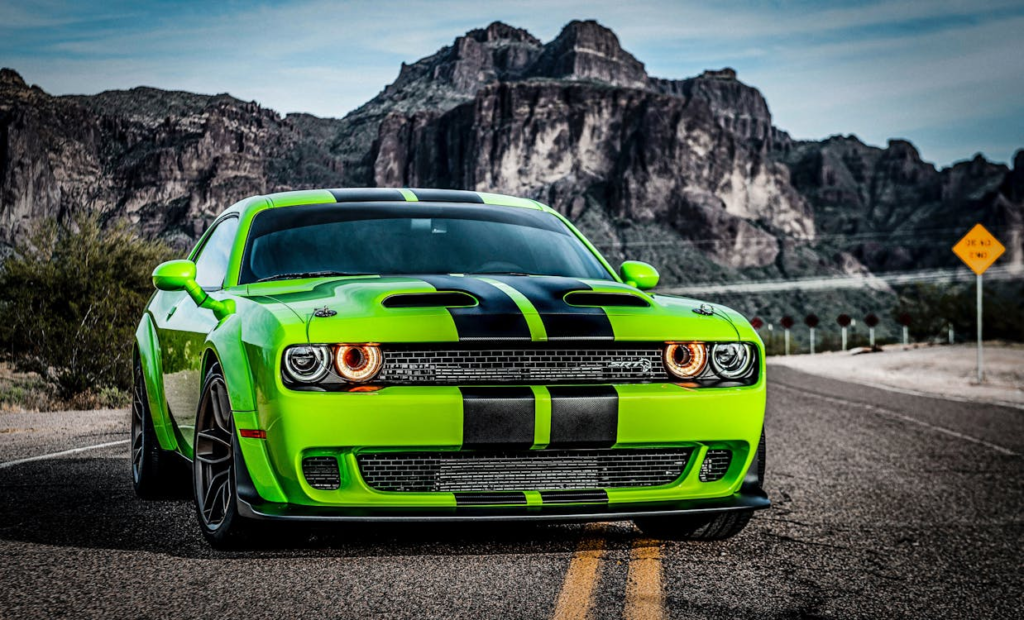 Bright green Dodge Challenger with black racing stripes on an open road.