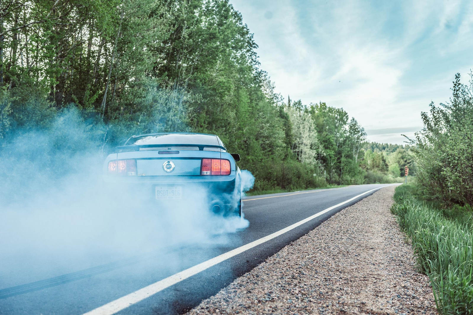 Classic hot rod car drifting with smoke on rural road.