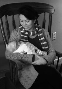 Portrait of Amber Mayhew holding a newborn on a rocking chair
