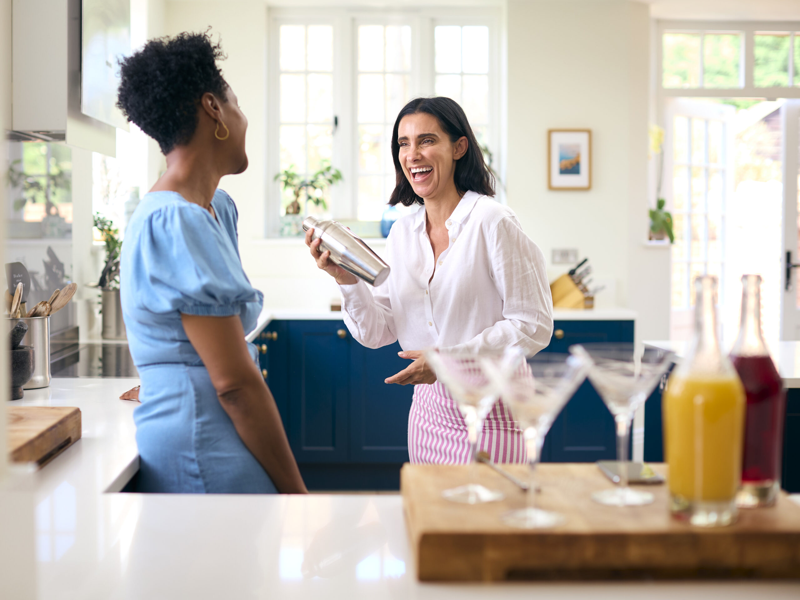 Two mature female friends at home having fun mixing cocktails together