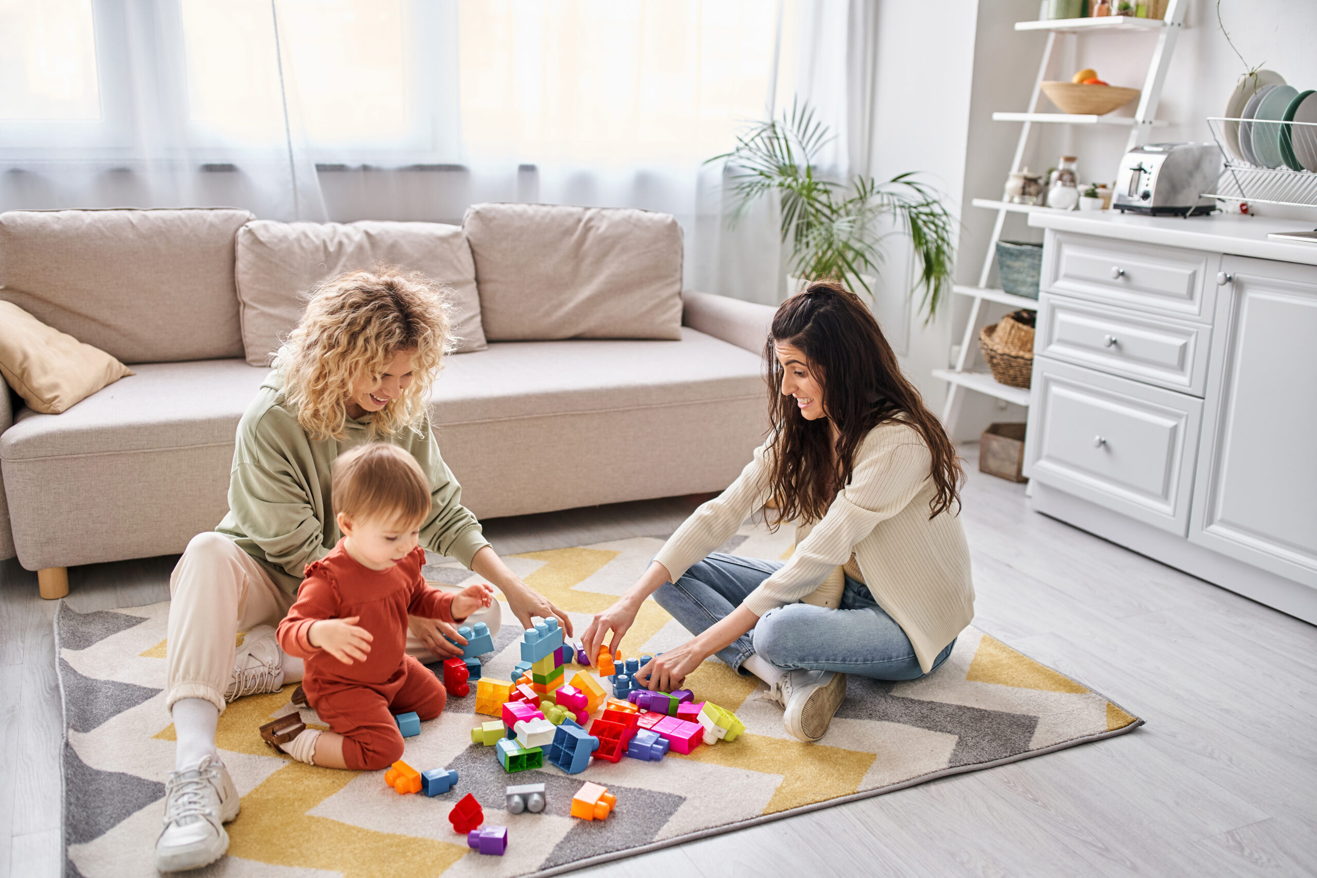 Cheerful caring lesbian couple playing with their toddler daughter at home, modern parenting