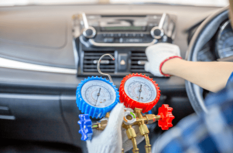 Technician recharging car air conditioning with gauges inside vehicle.