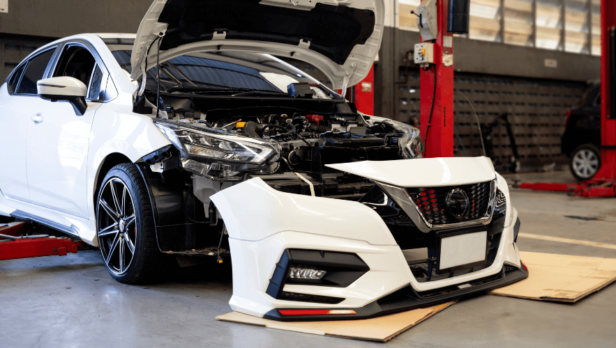 Modern white sedan with front-end damage in auto repair shop.
